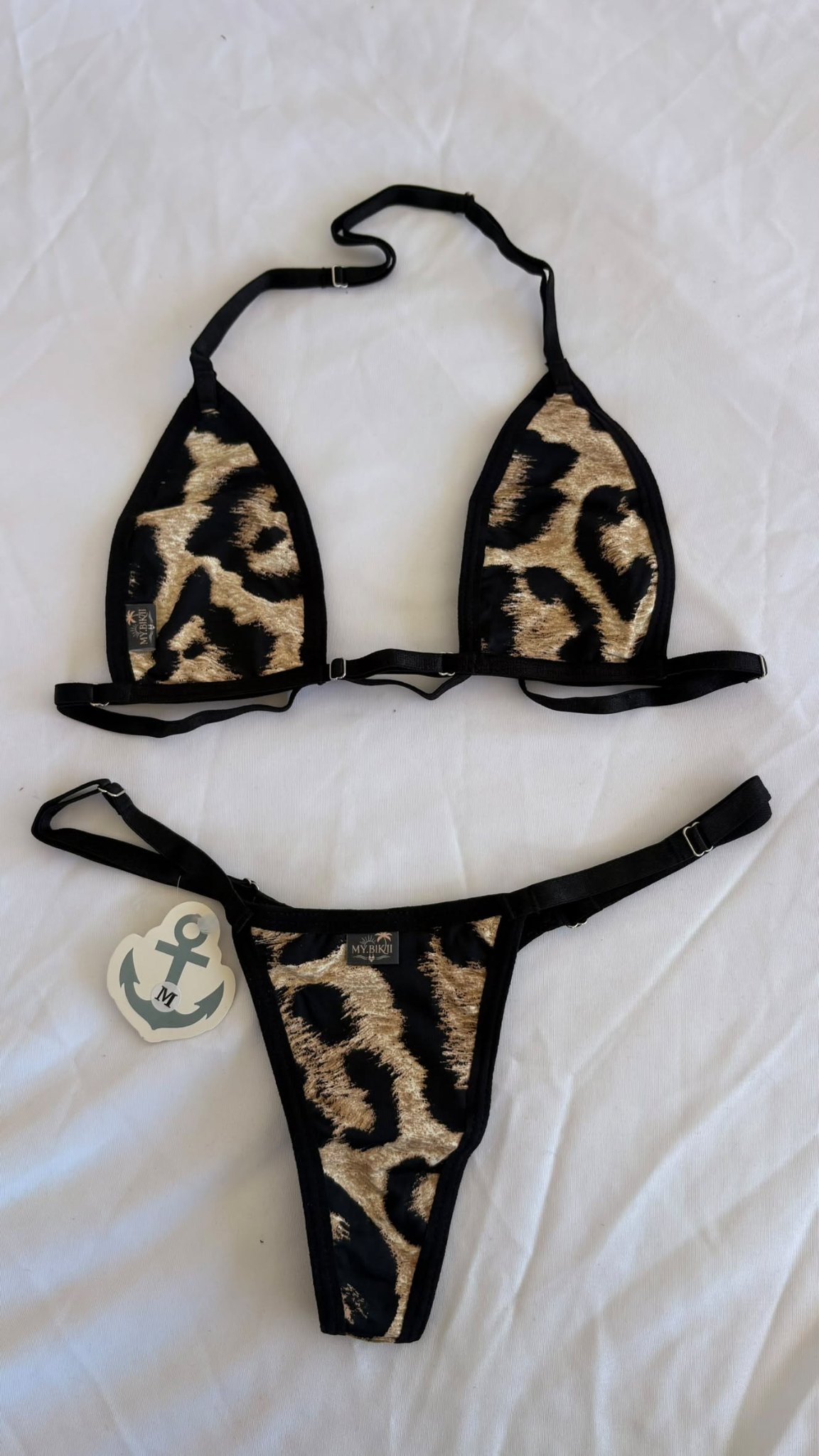 Ensemble bikini triangle à imprimé léopard beige et noir avec liserés noirs, posé à plat.